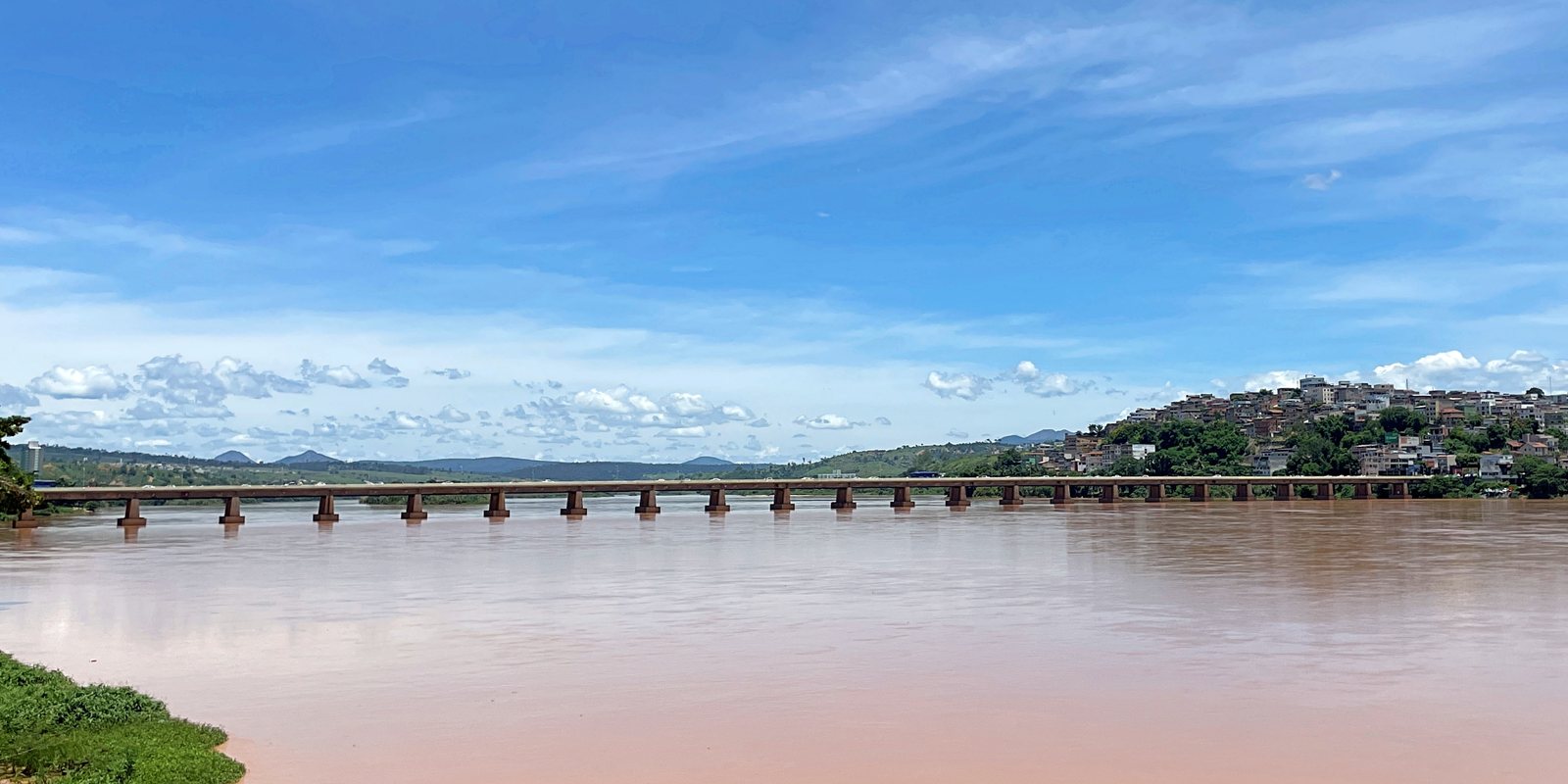 Ponte comprida sobre o rio Doce em Colatina, com a cidade na margem oposta e céu azul com nuvens esparsas